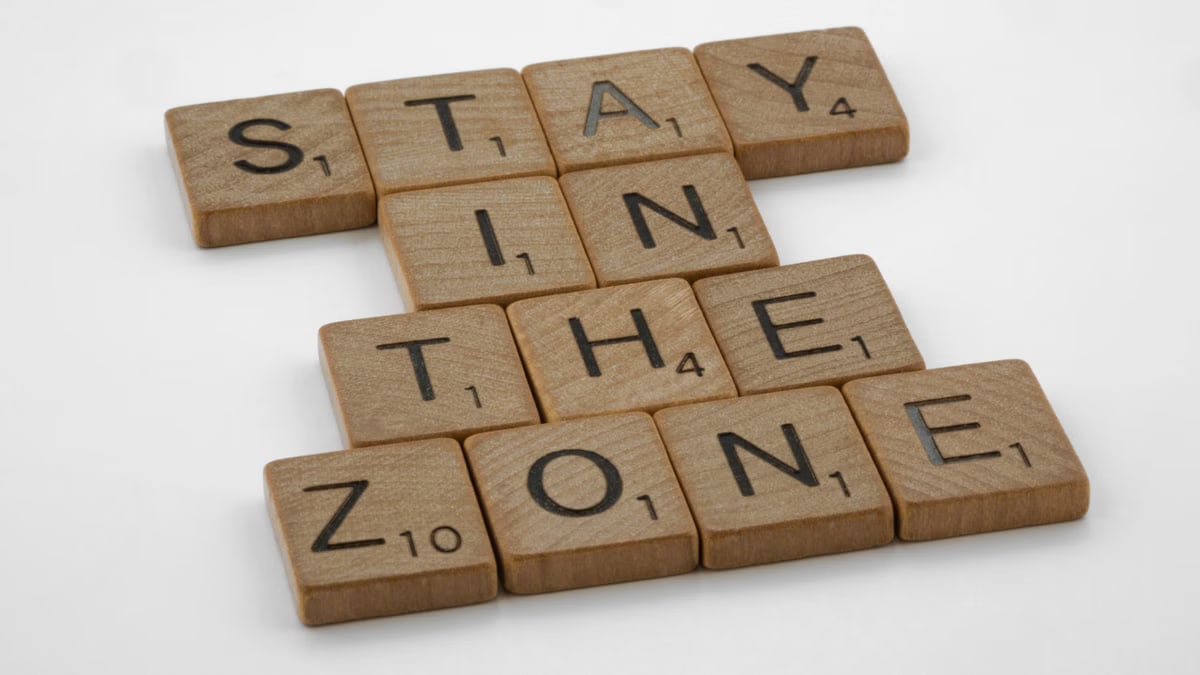 Wooden Scrabble tiles arranged to spell 'Stay in the Zone' on a white background.